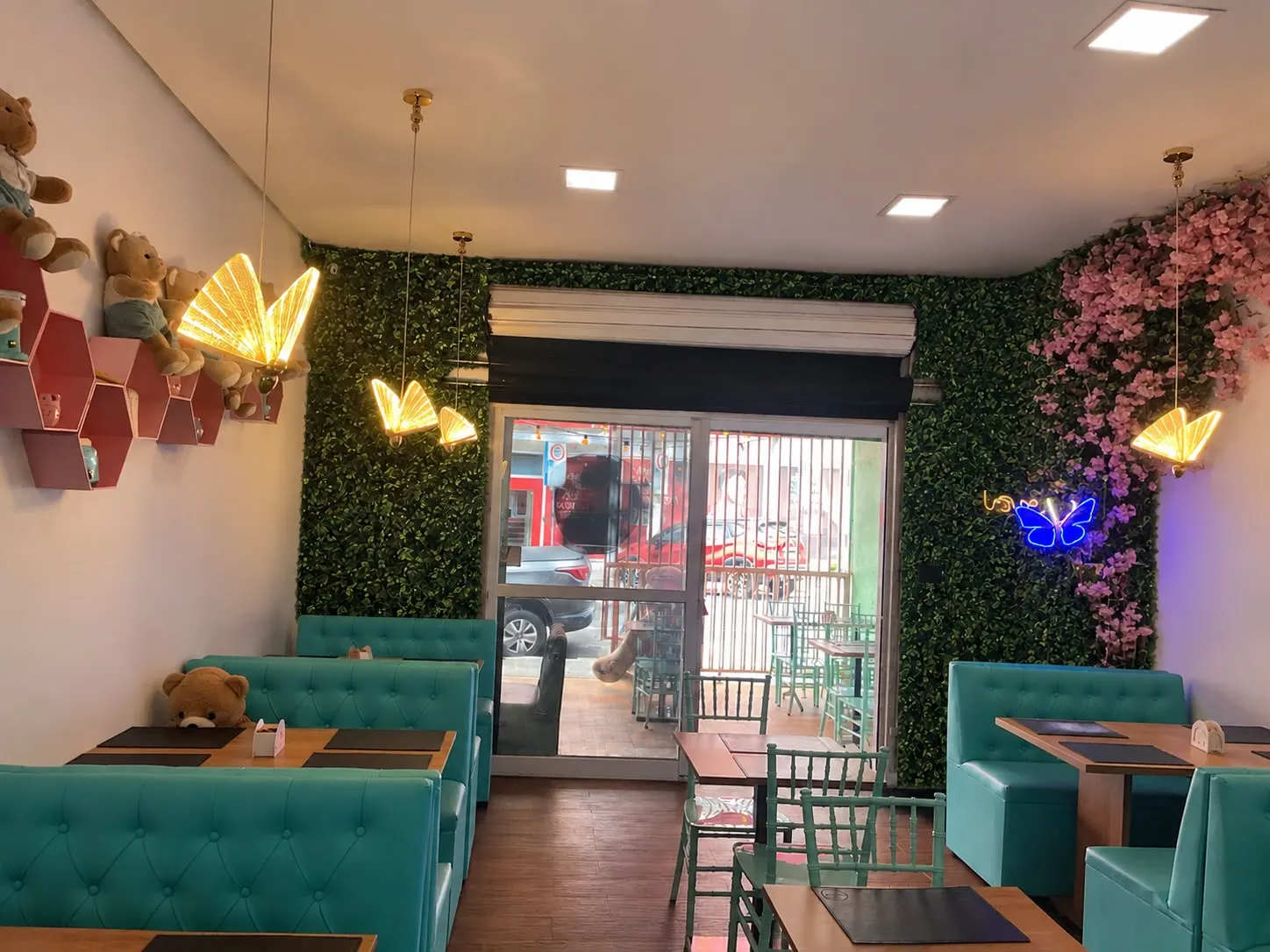 O salão da Cafeteria Dumont: sofás turquesa, parede de plantas e luminárias de borboleta